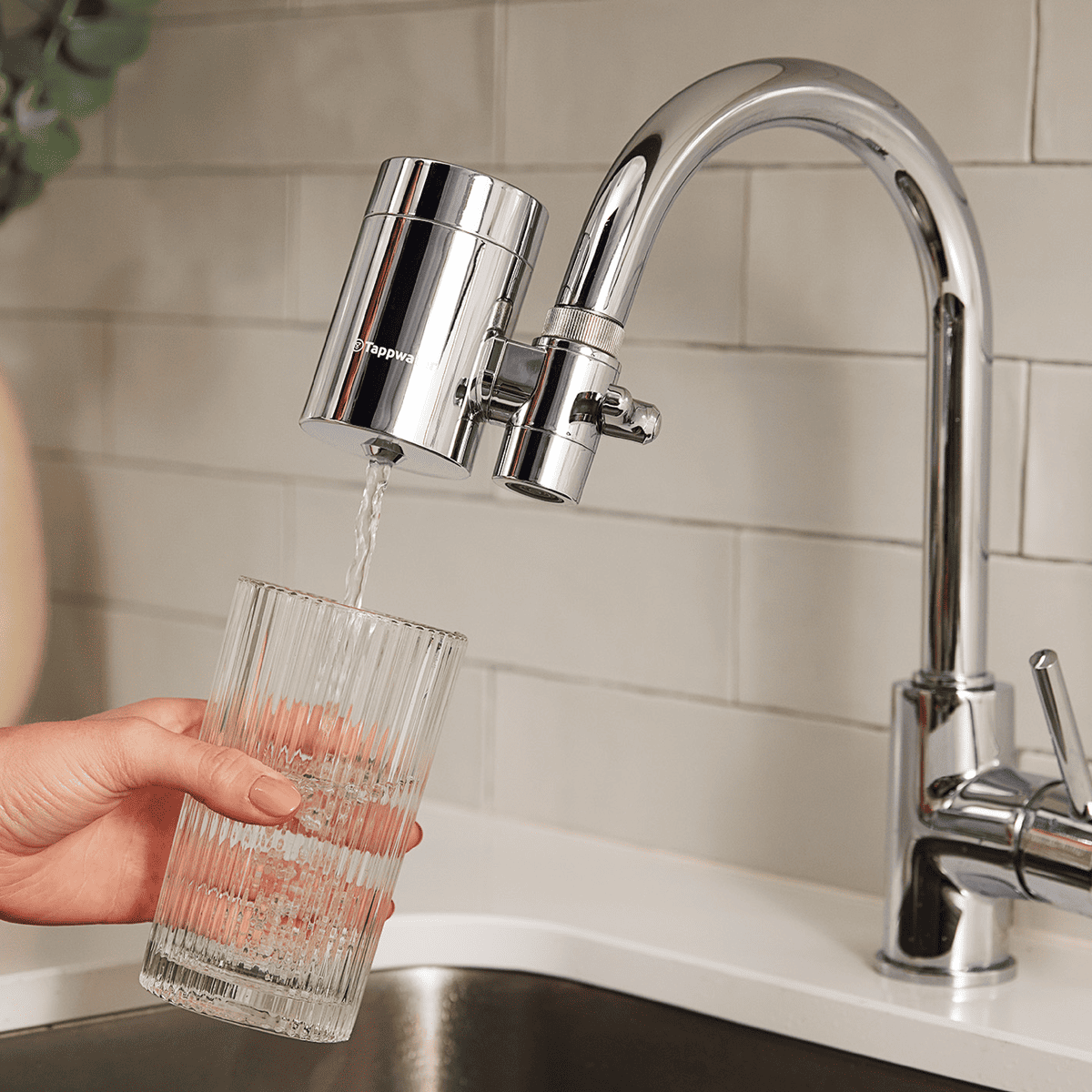 Person holding a glass under a kitchen faucet with a water filter attachment.