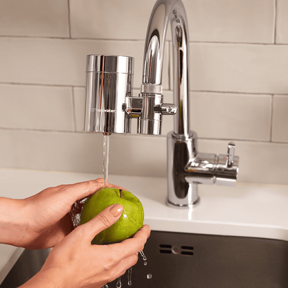 Person washing a green apple under running water from a kitchen faucet.